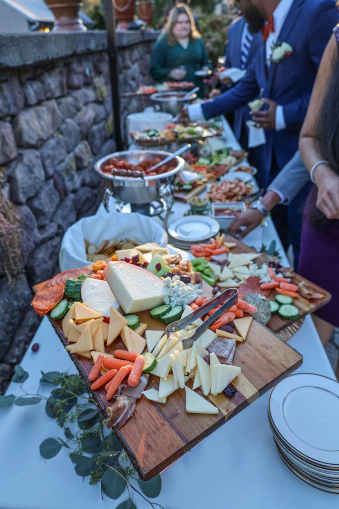 A vibrant outdoor buffet table displaying assorted cheeses, meats, and vegetables.
